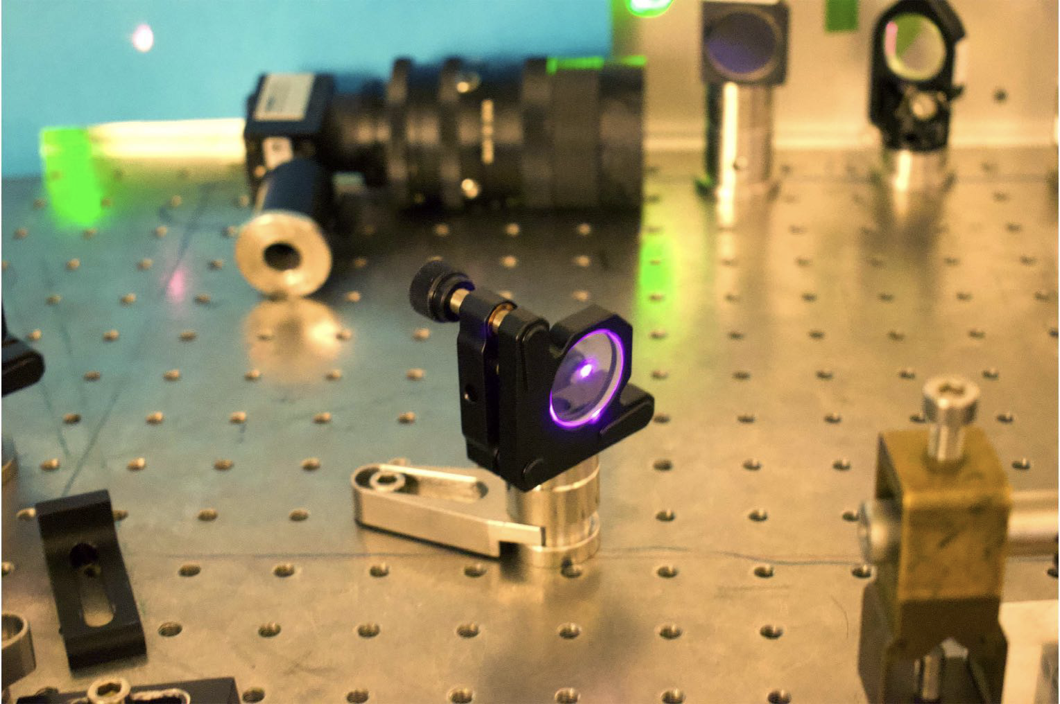 on the steel table there is a device with a lens which is reflecting purple-like laser light 
