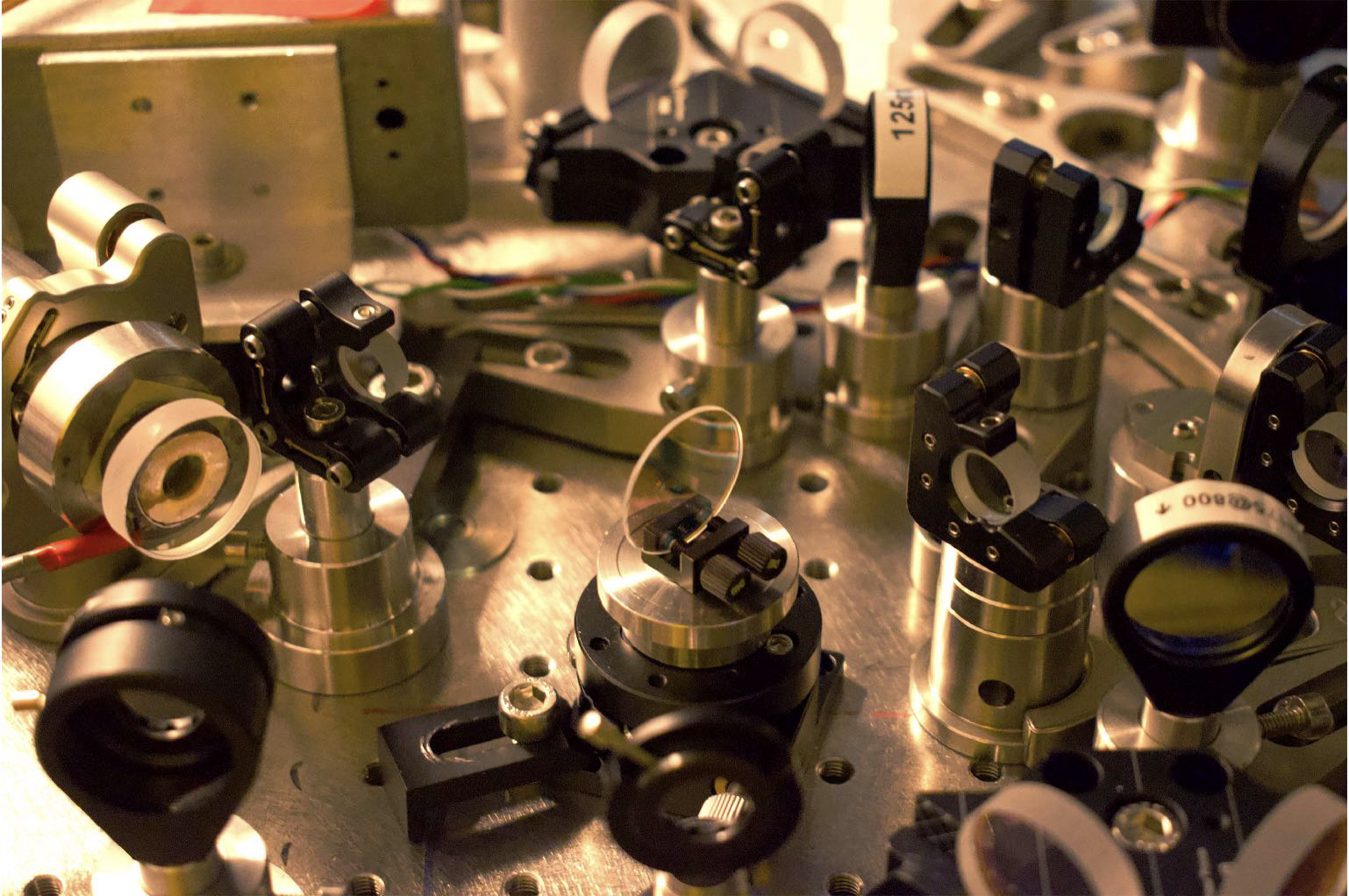 on the steel table among other metallic components there is a circular device that looks like a lens and it's called beam splitter