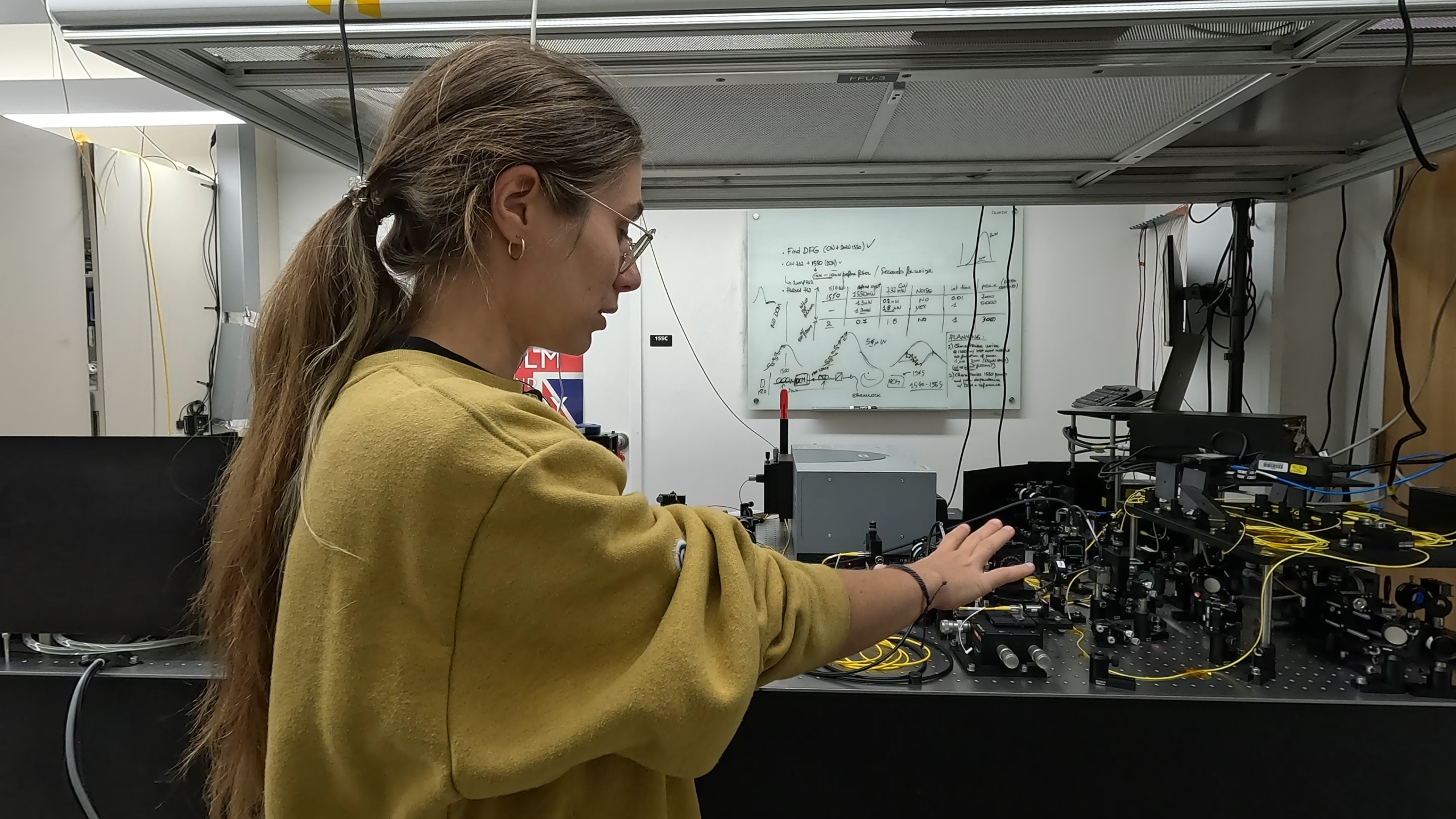 Researcher pointing at the optical table, as to explain the content of it